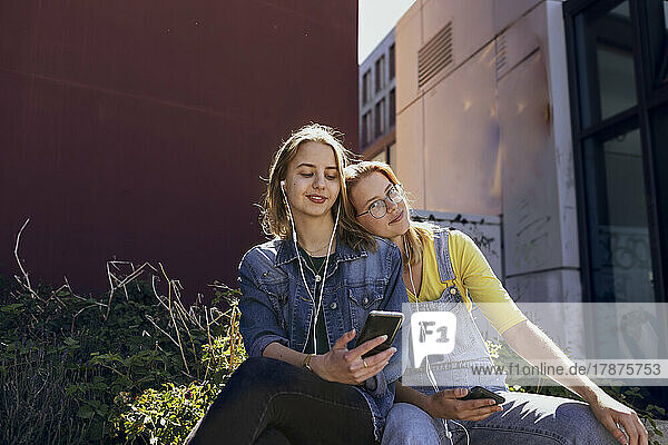 Young friends with smart phone listening music through in-ear headphones