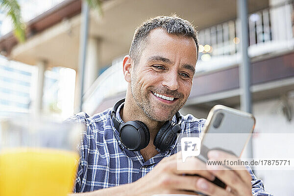 Happy mature man using mobile phone at outdoor cafe