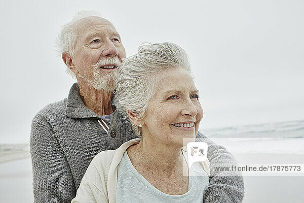 Happy senior couple standing smiling on windy beach