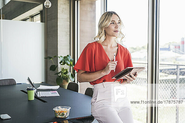 Thoughtful businesswoman with tablet PC at desk in office
