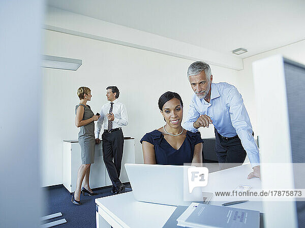 Mature businessman and businesswoman using laptop with colleagues discussing in office