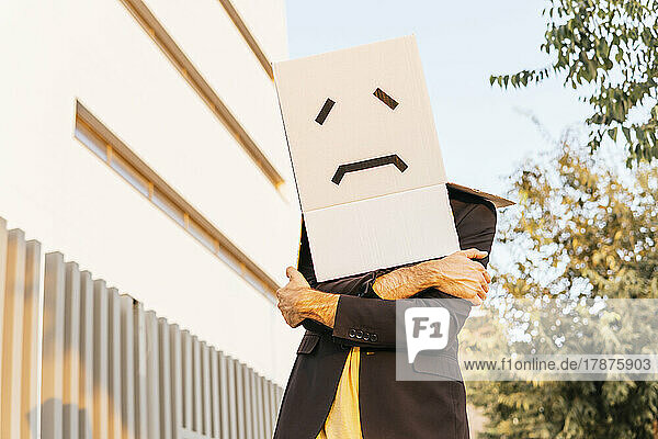 Man wearing box with sad face standing with arms crossed