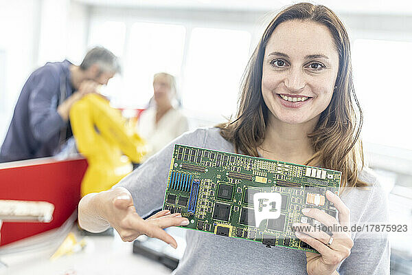 Smiling woman holding motherboard in factory