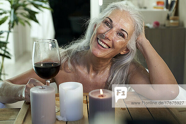 Happy woman with red wine in bathroom