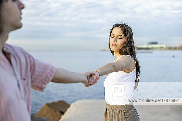 Young couple with eyes closed holding hands on pier