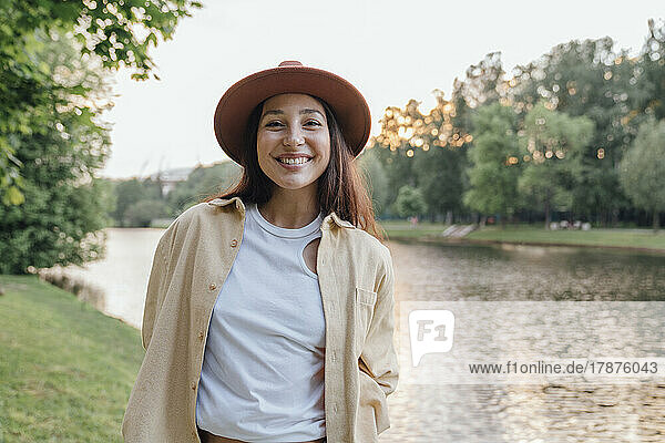 Cheerful woman in hat by lake in park