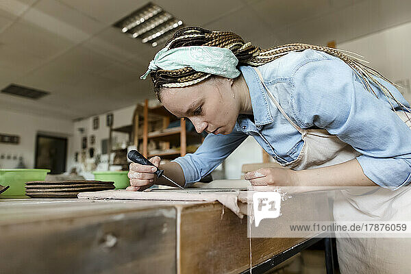 Young potter with hand tool working at art studio