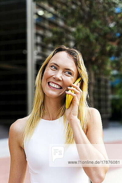 Happy woman talking through mobile phone on footpath