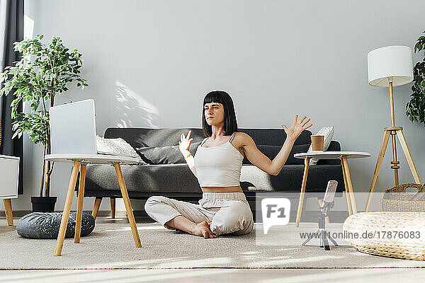 Woman with arms outstretched doing online yoga in front of laptop at home