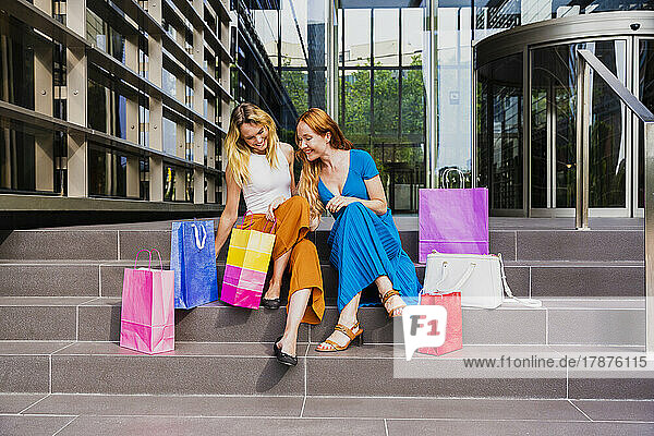 Woman peeking into friends shopping bag outside mall