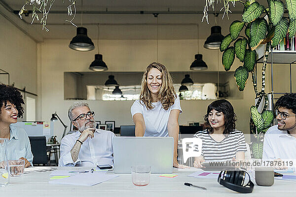 Lächelnde Geschäftsfrau plant Strategie am Laptop mit Kollegen im Büro