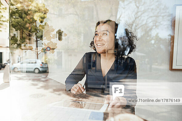 Smiling woman with tablet PC seen through glass of cafe