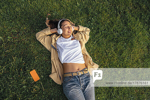 Woman with hands behind head lying on grass at park