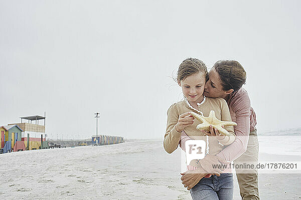 Mother kissing daughter on the beach holding starfish