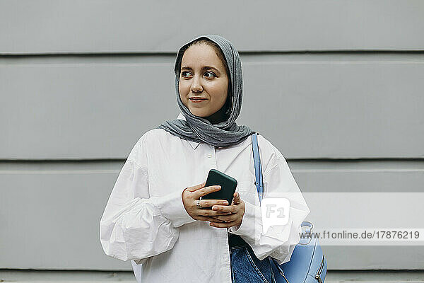 Lächelnde junge Frau mit Hijab steht vor der Wand