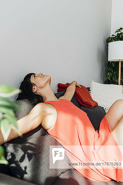 Woman with arms outstretched relaxing on sofa at home