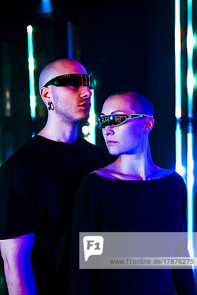 Man and woman wearing smart glasses in front of neon lighting