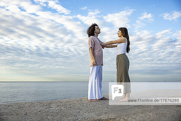 Young couple touching each other standing on pier by sea