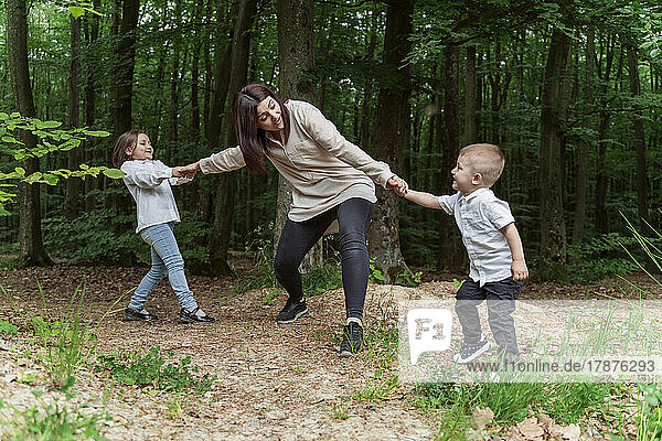 Happy children pulling mother having fun in forest