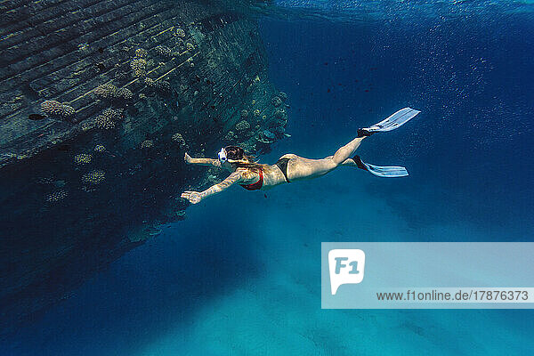 Frau schwimmt unter Wasser an einem Schiffswrack vorbei