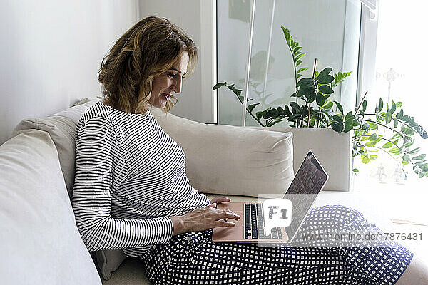 Woman sitting on sofa using laptop in living room at home