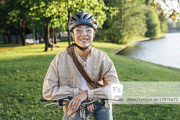 Smiling woman with helmet sitting on bicycle at park