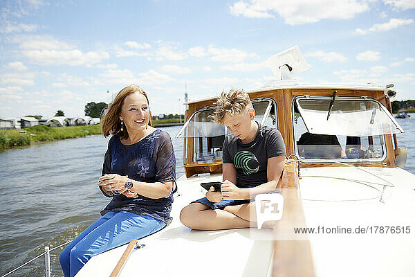 Smiling grandmother with grandson using smart phone sitting cross-legged on boat deck