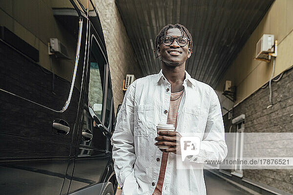 Smiling young man with disposable coffee cup standing by van