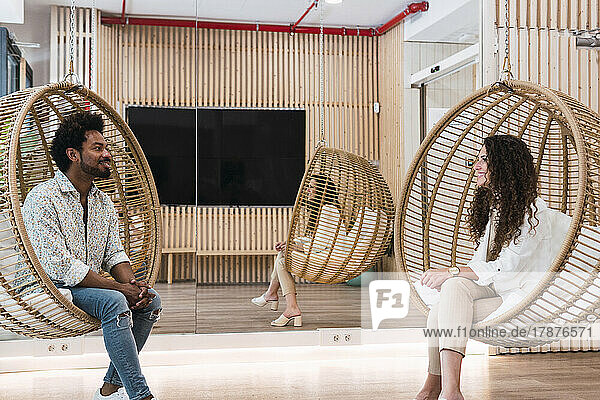Businessman and businesswoman sitting in hanging chairs talking to each other