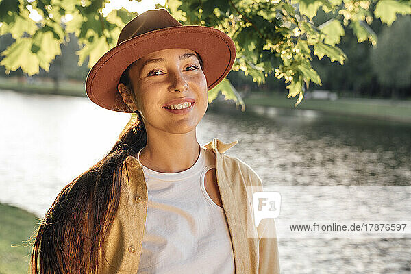 Smiling woman with hat standing in front of lake