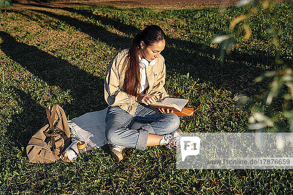 Frau sitzt auf Gras und liest Buch im Park