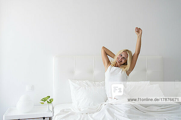 Smiling woman stretching arms sitting on bed