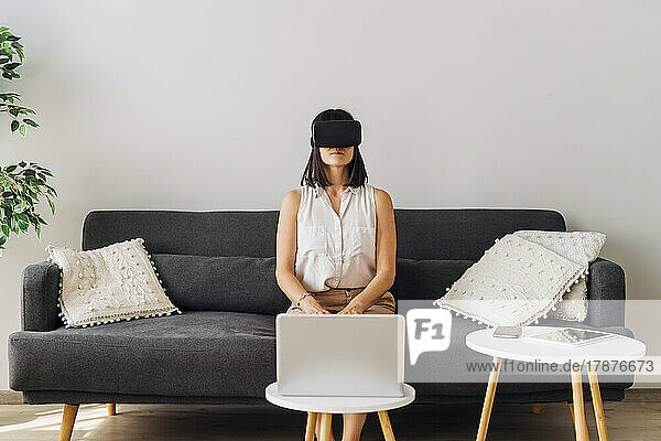 Woman using virtual reality glasses sitting on sofa at home