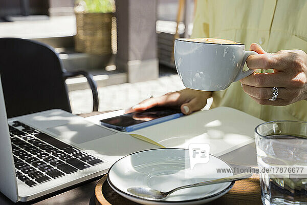 Hand of freelancer holding coffee cup at sidewalk cafe