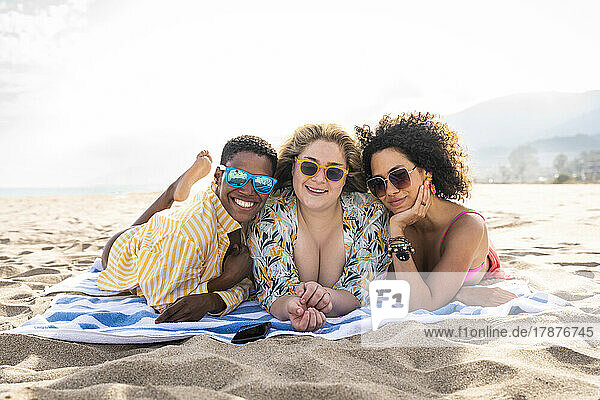 Multiracial friends with sunglasses lying on towel at beach