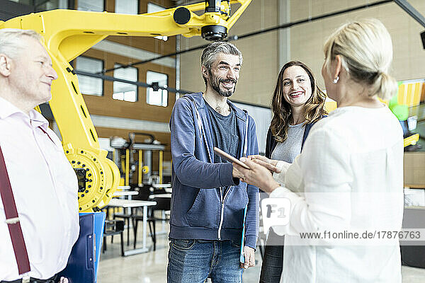 Technicians shaking hands with senior colleague at meeting in factory with industrial robots