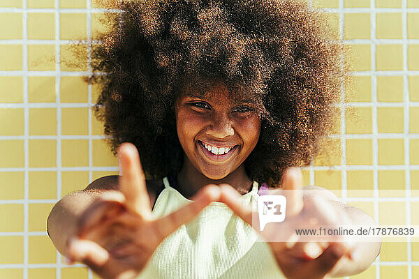 Lächelndes Mädchen mit Afro-Frisur  das ein Friedenszeichen zeigt