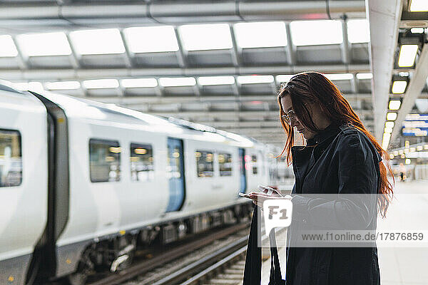 Redhead woman using smart phone at railroad station platform
