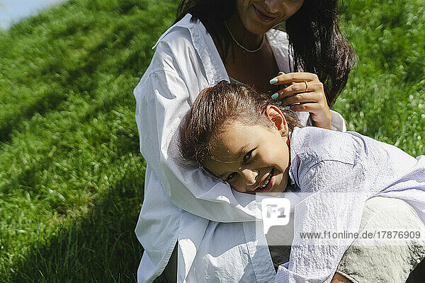 Smiling girl leaning on mother on meadow