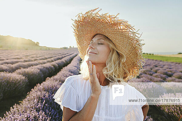 Lächelnde Frau mit geschlossenen Augen  die ihr Kinn im Lavendelfeld berührt