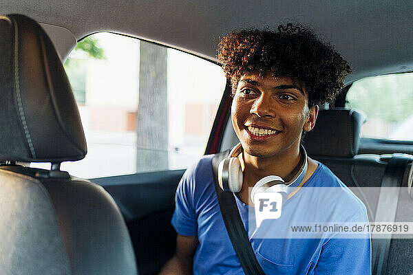 Lächelnder Mann mit kabellosen Kopfhörern sitzt im Auto