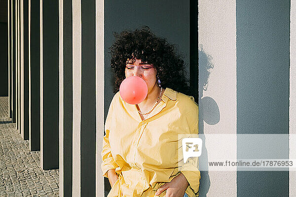 Young woman blowing bubble gum by column