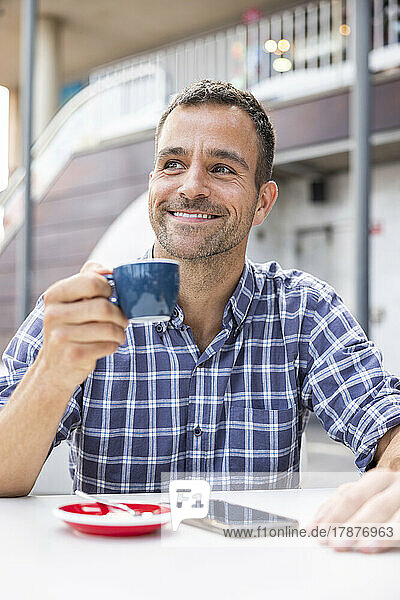 Smiling mature man drinking coffee at sidewalk coffee