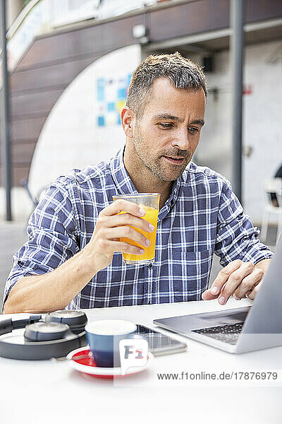Mature freelancer with orange juice using laptop at cafe
