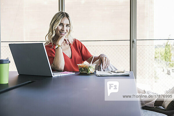 Businesswoman sitting with laptop and lunch box at desk in office
