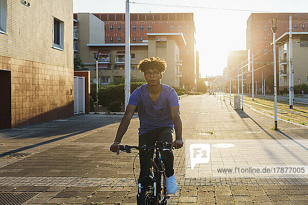 Young man riding bike in city at sunset