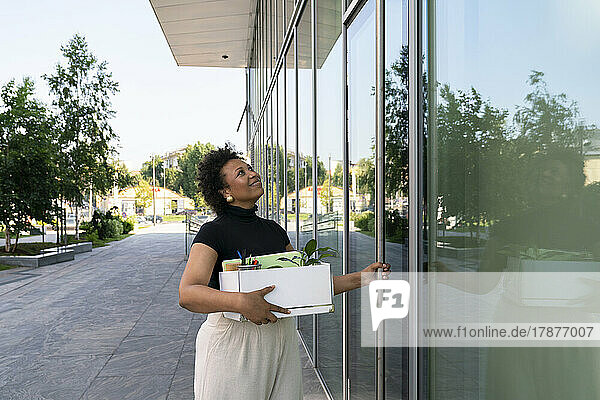 Smiling businesswoman holding box opening glass door