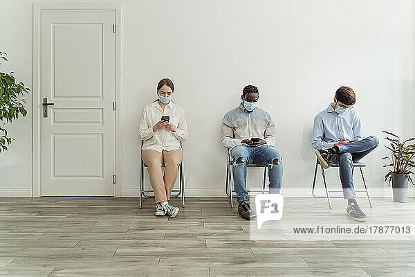 Menschen mit Gesichtsmasken sitzen auf Stühlen im Wartebereich