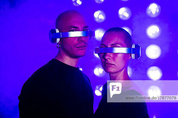 Couple wearing futuristic glasses with headphones by glowing lights