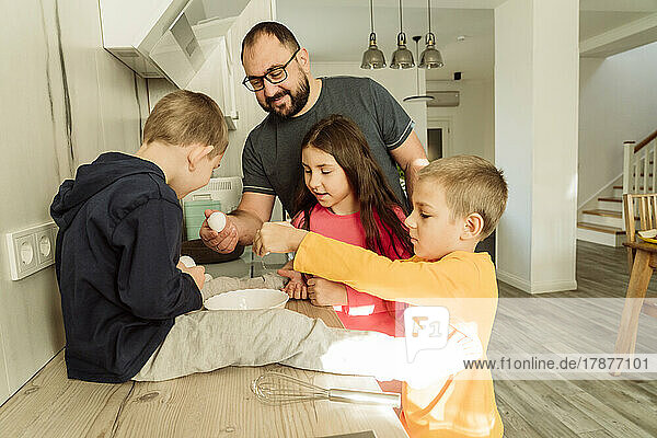 Smiling man with children preparing breakfast in kitchen